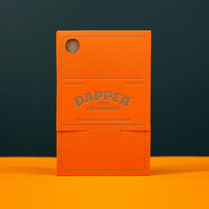 orange paper packaging for a pocket notebook standing on a yellow tabletop. the packaging reads &